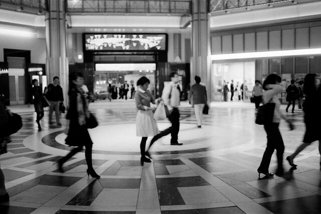 Black and white: people crossing a station concourse, blurred by a slow shutter